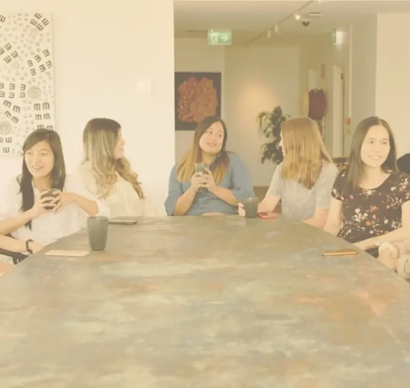 Group of women sitting around a table in a room, each holding a mobile phone in their hands